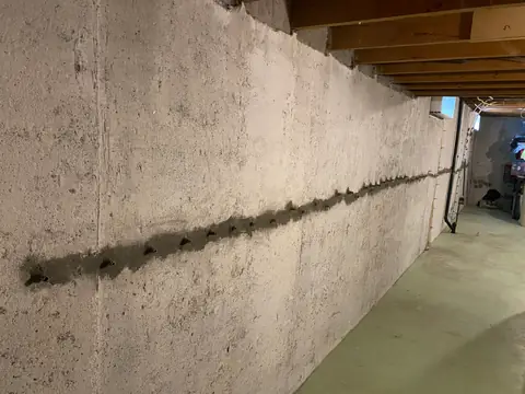 Wide basement wall view with a long horizontal treated line beneath timber joists