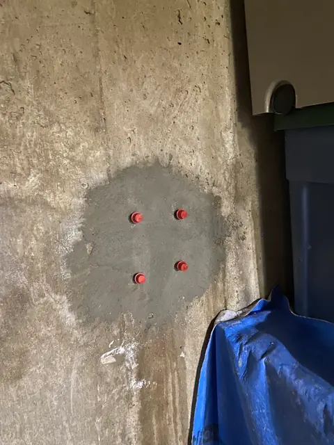 Four red-capped ports within a darker prepared patch on a concrete wall