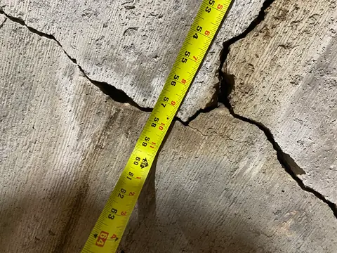 Tape measure beside a close view of intersecting concrete cracks