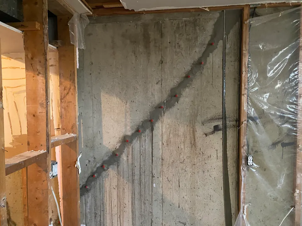 Diagonal prepared crack with red repair ports on an exposed concrete wall