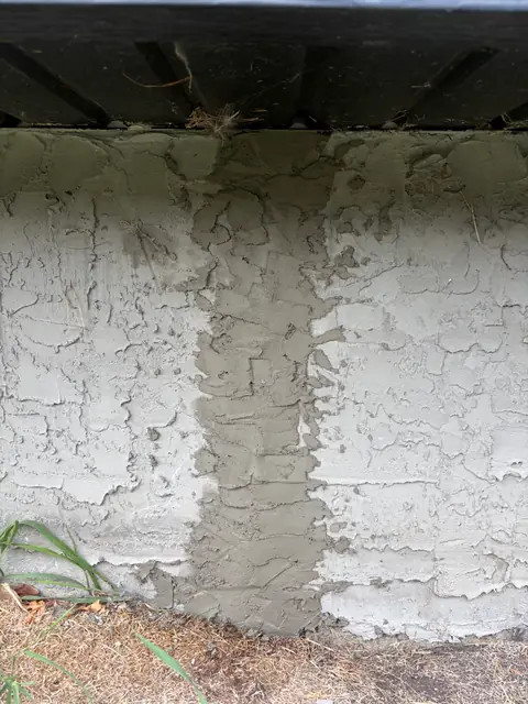 Exterior foundation wall with a vertical patched area above the ground