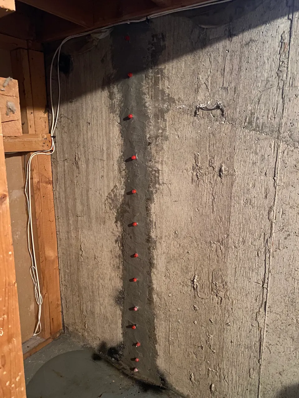 Red-capped repair ports along a vertical concrete wall line beside timber framing