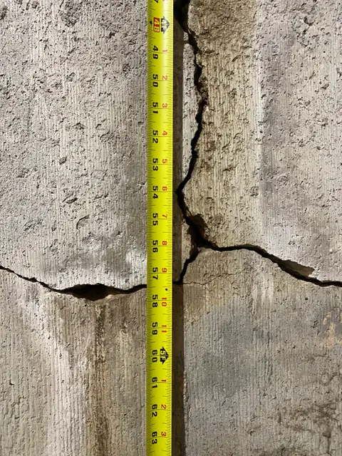 Crossing concrete cracks with a vertical yellow measuring tape alongside