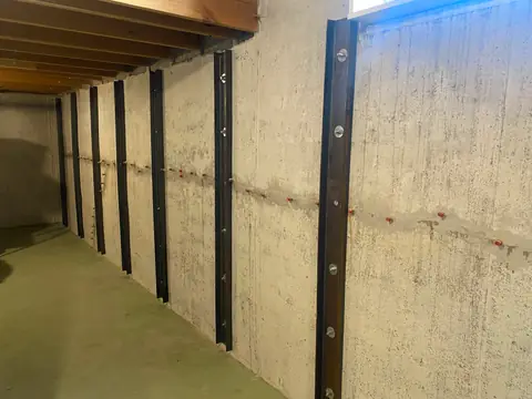 Exposed basement wall with vertical steel members and an upper window