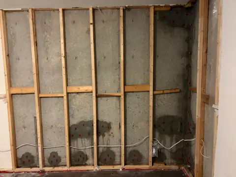 Opened basement wall with timber studs and prepared patches on exposed concrete