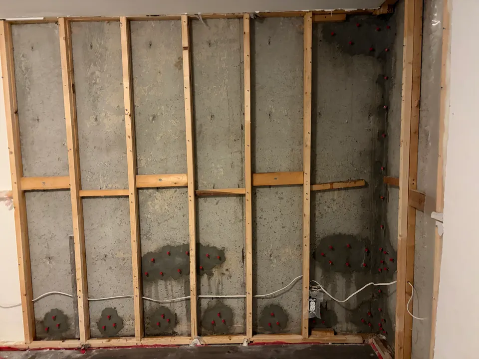 Opened basement wall with timber studs and prepared patches on exposed concrete
