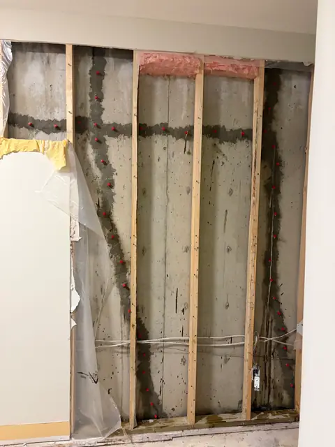 Wide view of an opened wall showing timber studs and concrete behind them