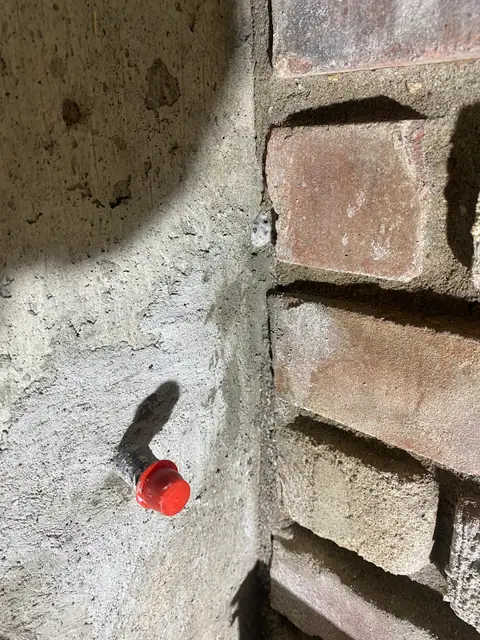 Close view of a red repair port in concrete beside brickwork