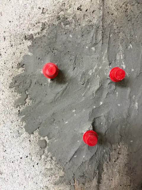 Close view of three red-capped repair ports in a prepared concrete surface