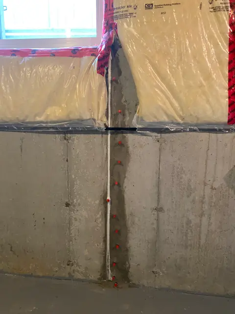 Vertical concrete repair line below a basement window and exposed insulation