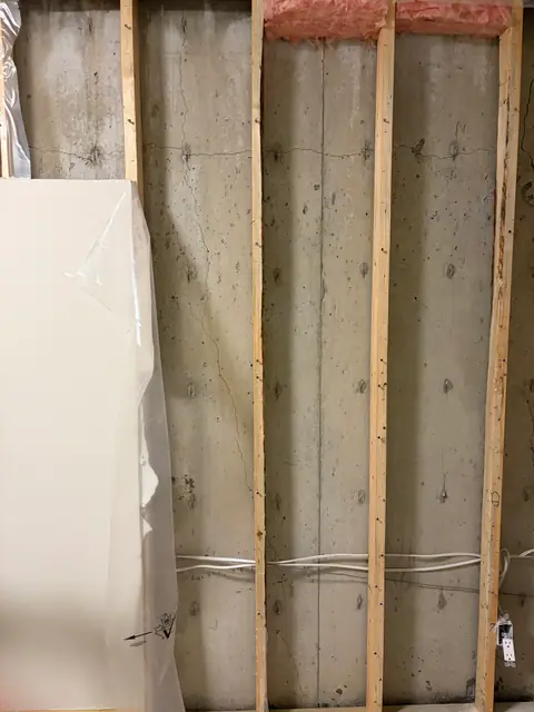 Concrete wall visible through timber studs with wall finish opened at one side