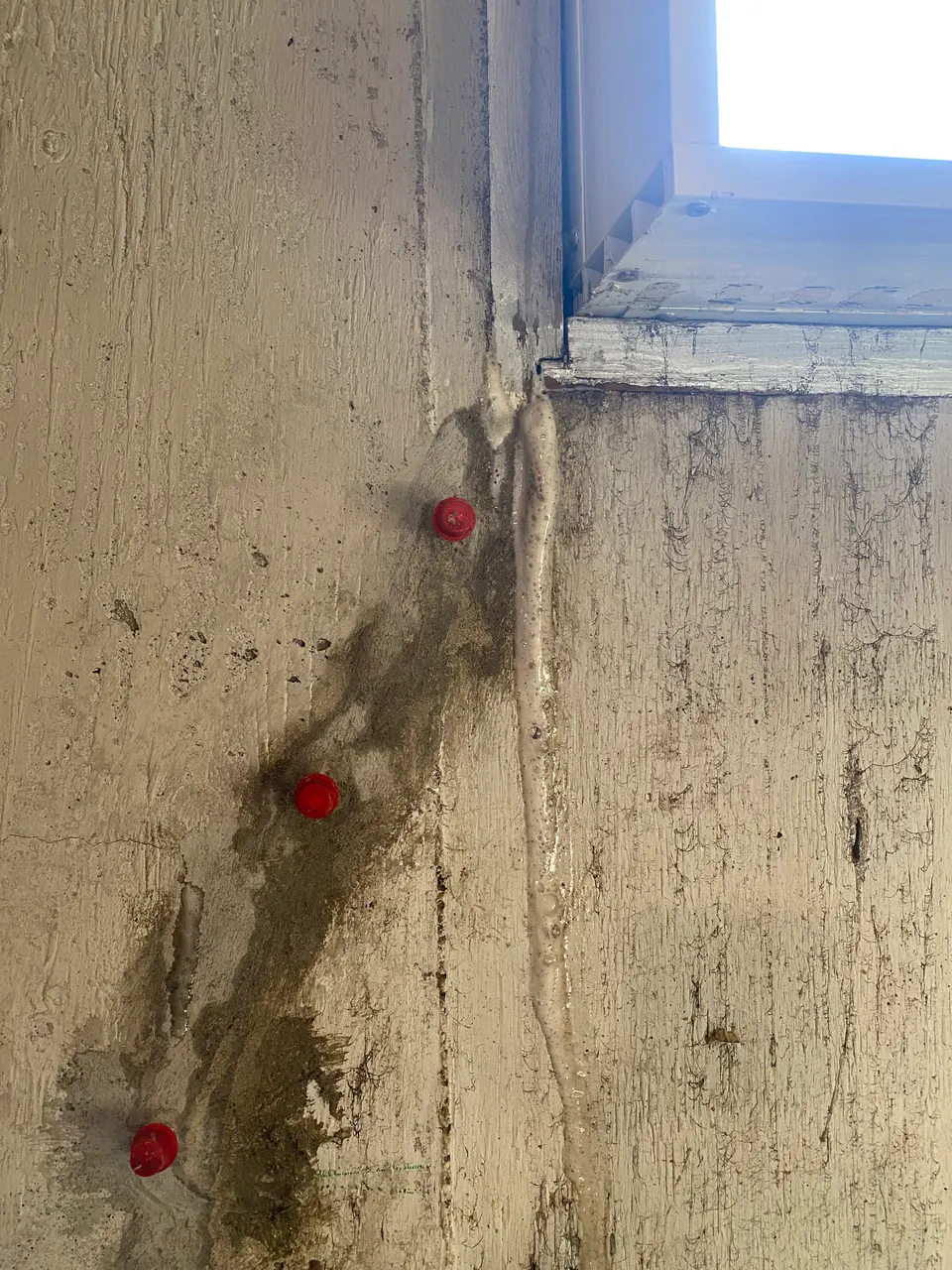 Red repair ports along a prepared crack beside a basement window