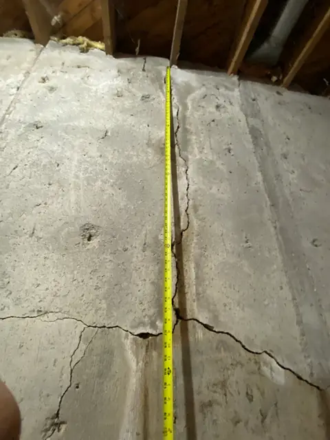 Vertical tape measure against a cracked concrete wall beneath floor joists