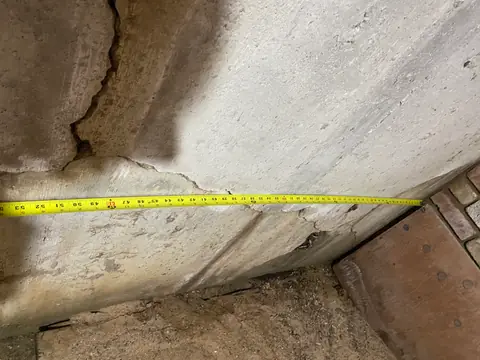 Yellow tape measure across a concrete wall with an irregular vertical crack